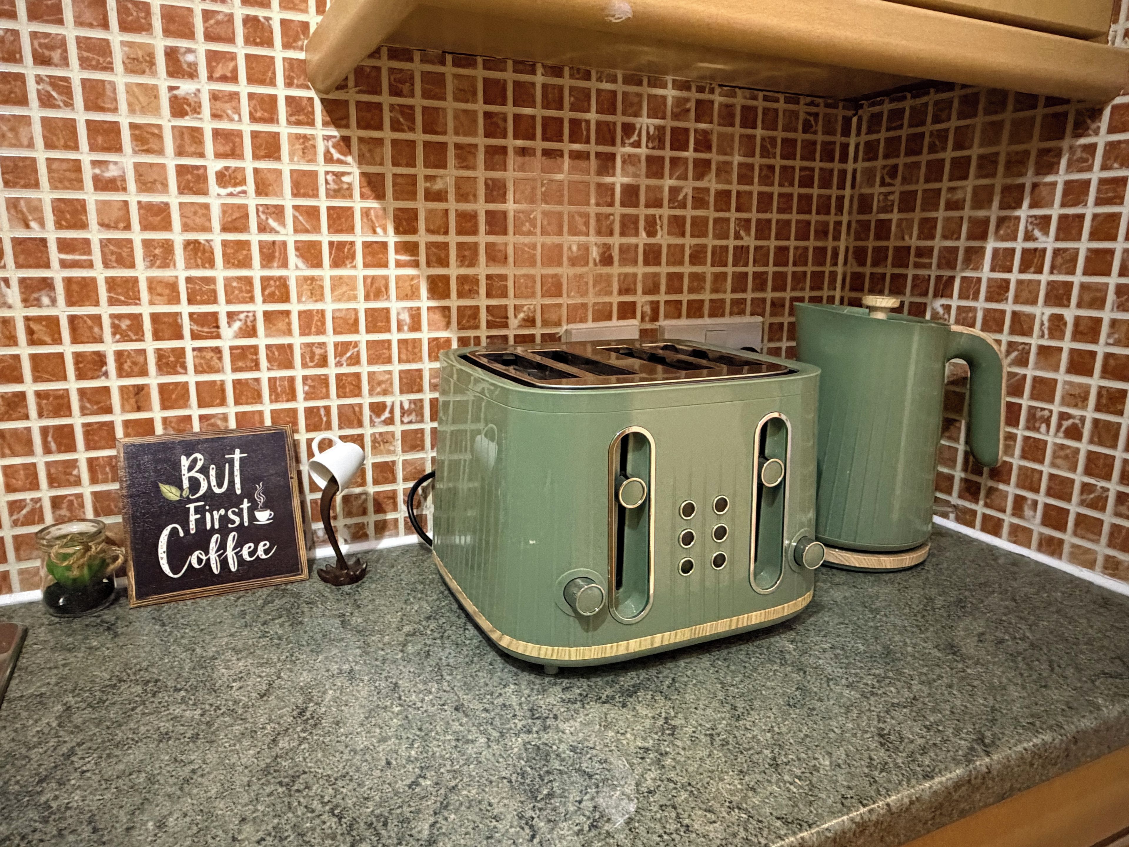 A kitchen with a green toaster and a kettle on the counter, a sign that reads 'But First Coffee,' and a small decorative item.