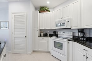 A kitchen with white cabinets, a microwave, an oven, and a coffee maker. - PICKED TOP BONITA CONDO, 85" SMART TV. RESORT POOL VIEW (Bonita Springs)
