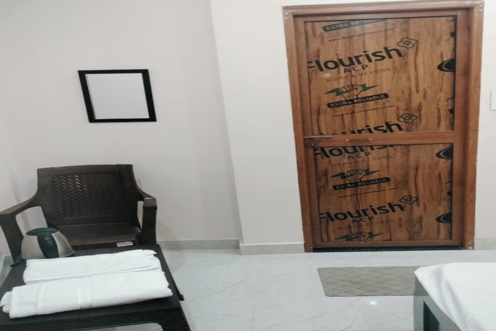 Una habitación de hotel con una puerta de madera, una silla negra y una cama con cubrecama blanca.