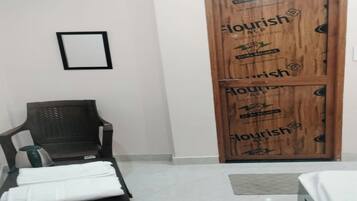 Una habitación de hotel con una puerta de madera, una silla negra y una cama con cubrecama blanca.