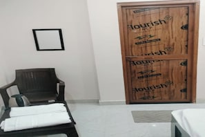Una habitación de hotel con una puerta de madera, una silla negra y una cama con cubrecama blanca.