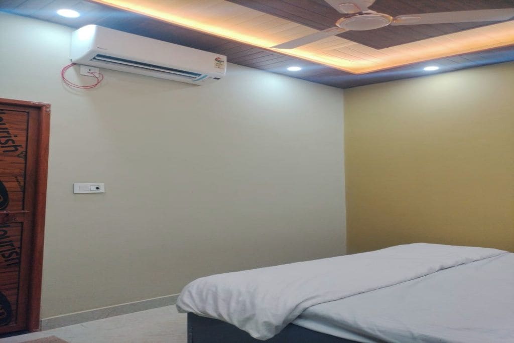 Un dormitorio con cama, unidad de aire acondicionado, ventilador de techo y una puerta con picaporte circular.