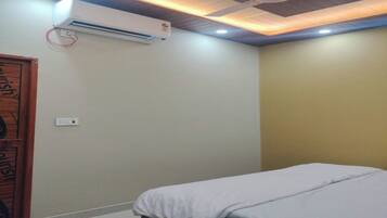 Un dormitorio con cama, unidad de aire acondicionado, ventilador de techo y una puerta con picaporte circular.