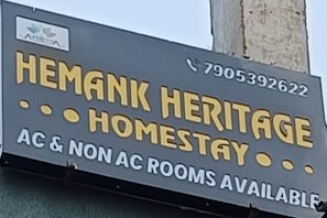 Letrero de Hemank Heritage Homestay que anuncia habitaciones con y sin aire acondicionado.