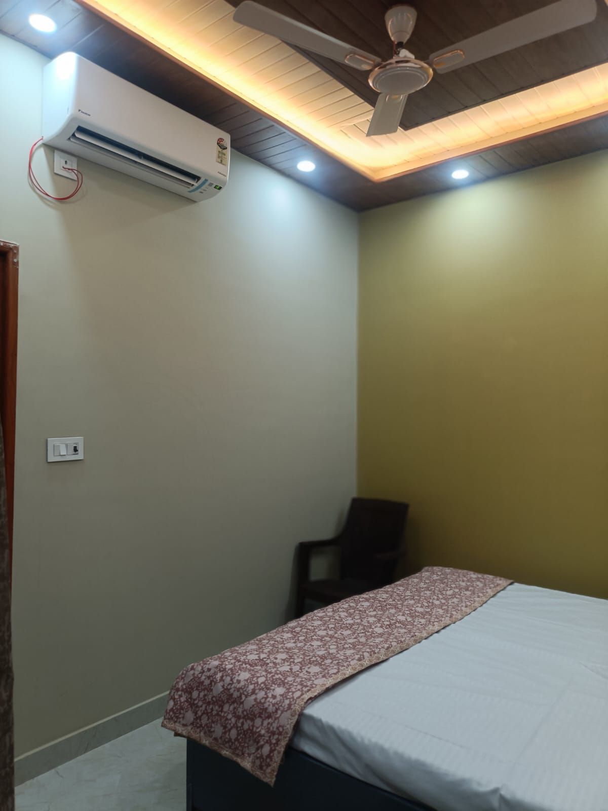 A bedroom with a bed, a ceiling fan, an air conditioner, and a chair.