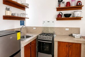 Cucina con piano cottura a gas, forno, frigorifero in acciaio inossidabile ed scaffali in legno con stoviglie.
