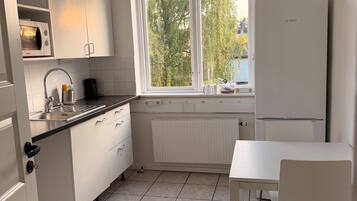 Una cocina con armarios blancos, una ventana, un radiador y una mesa blanca.