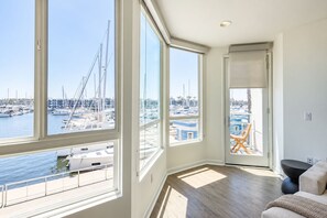 A spacious room with large windows overlooking a marina, a modern black sofa, and a wooden deck. - Coral Marina' Water Views Pool Jacuzzi Sauna Gym (Marina del Rey)