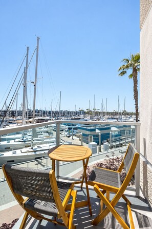 A balcony with two chairs and a small table, overlooking a marina with multiple boats. - Coral Marina' Water Views Pool Jacuzzi Sauna Gym (Marina del Rey)