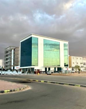 A modern building with a large glass facade, a flat roof, and a parking lot in front. - Lavender Hotel Apartrment (Tabuk)