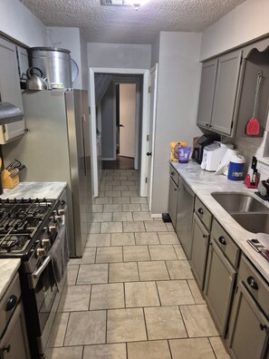 A kitchen with a stove, refrigerator, and cabinets. There is a hallway leading to another room. - Serene 1-bedroom house with AC in Tulsa perfect for relaxing (Tulsa)