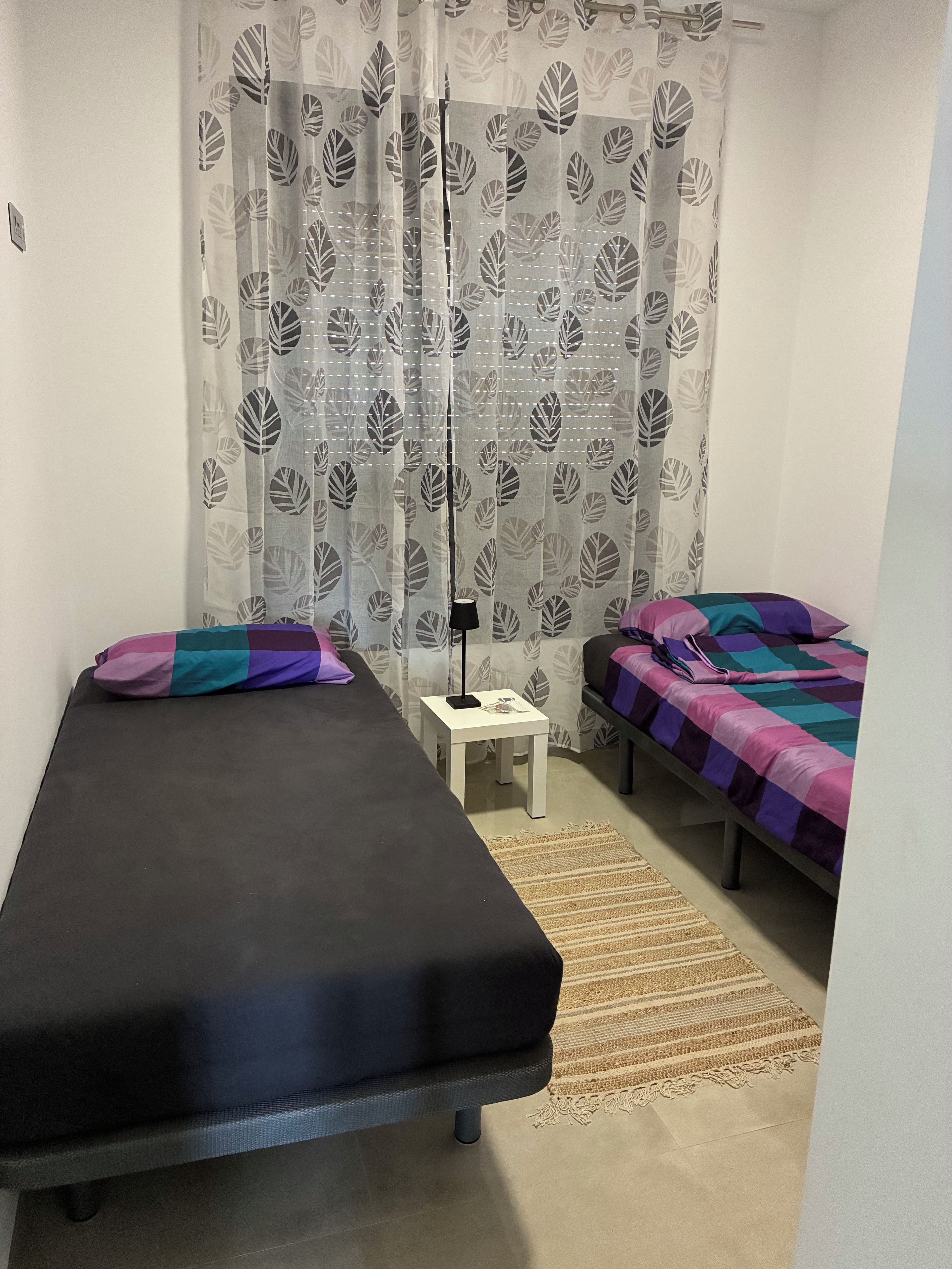 A bedroom with two beds, a small white table, and a patterned curtain.