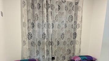 A bedroom with two beds, a small white table, and a patterned curtain.