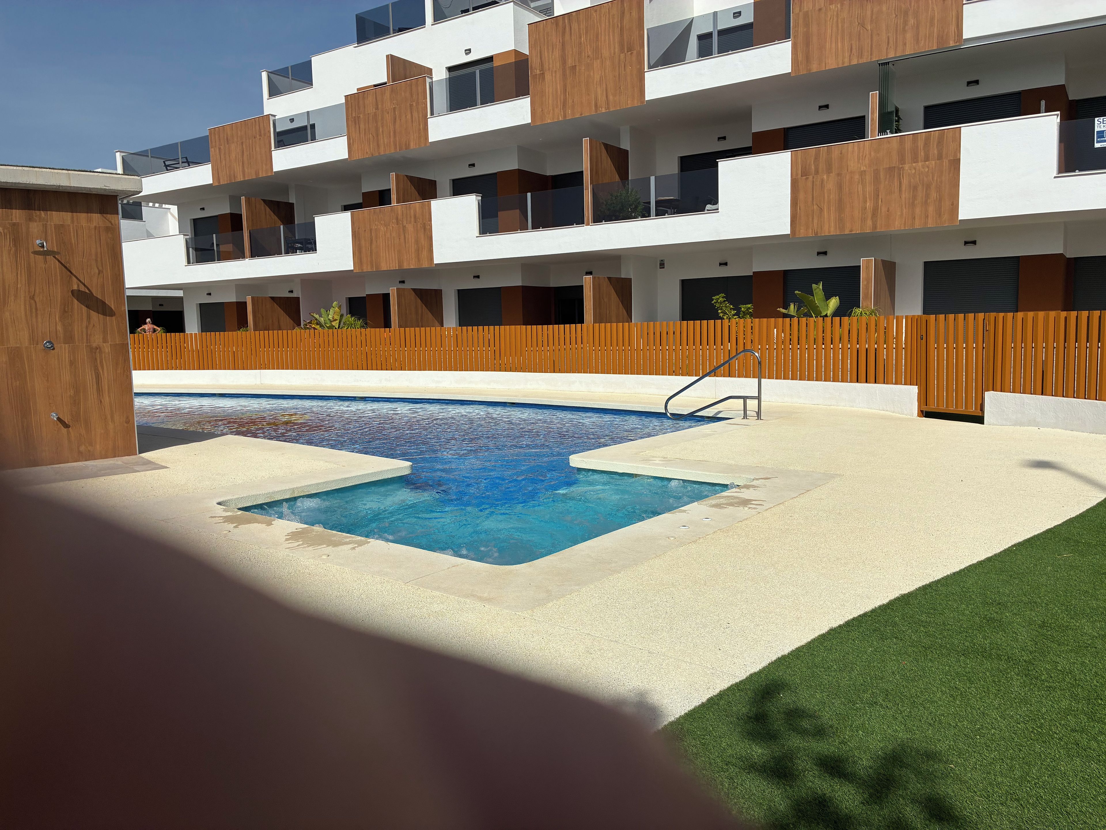 A modern building with a swimming pool, wooden deck, and a fenced area.