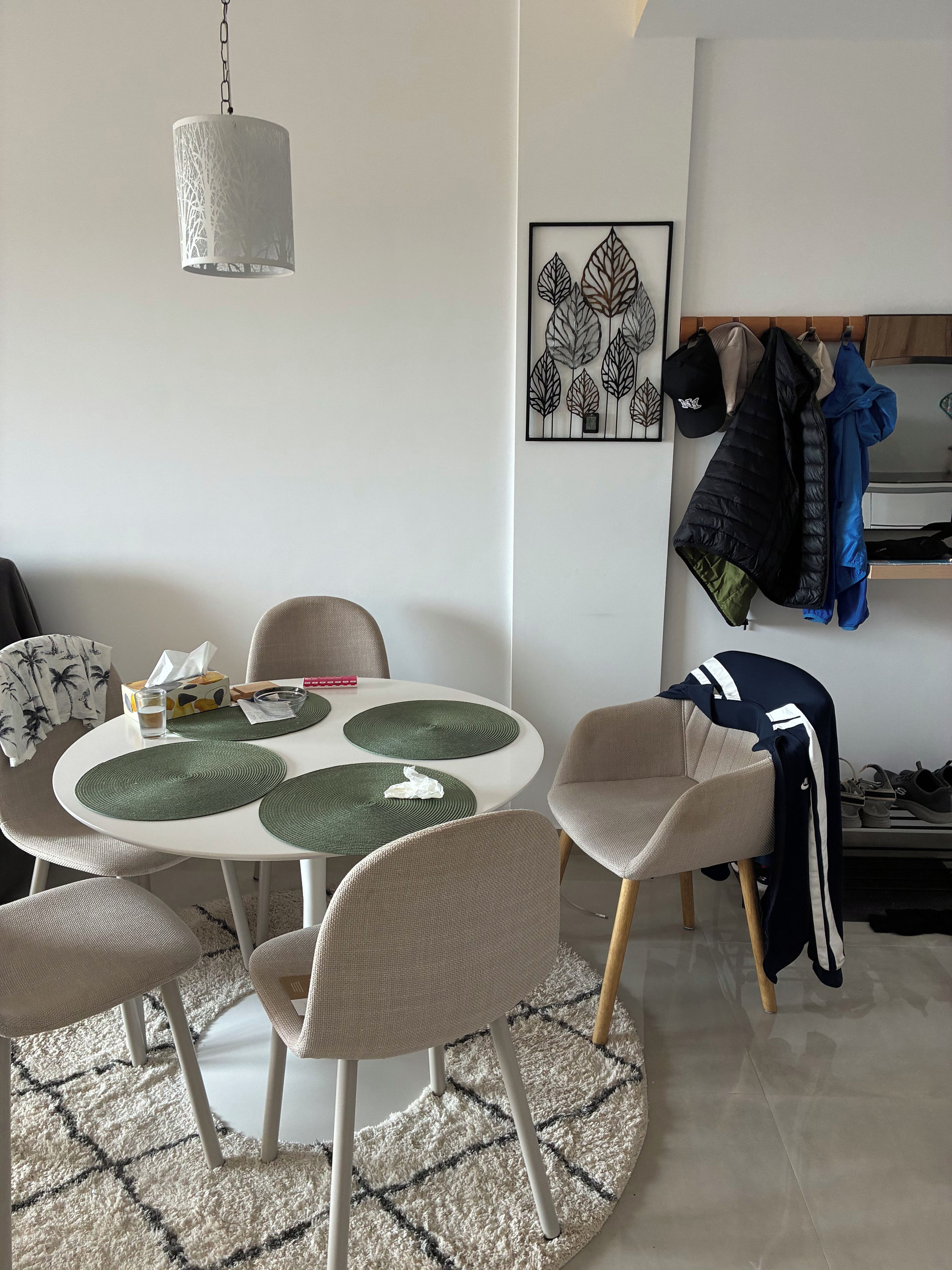 Een eetgedeelte met een ronde tafel, stoelen, een hanglamp, een decoratief kunstwerk aan de muur en een kledingrek.