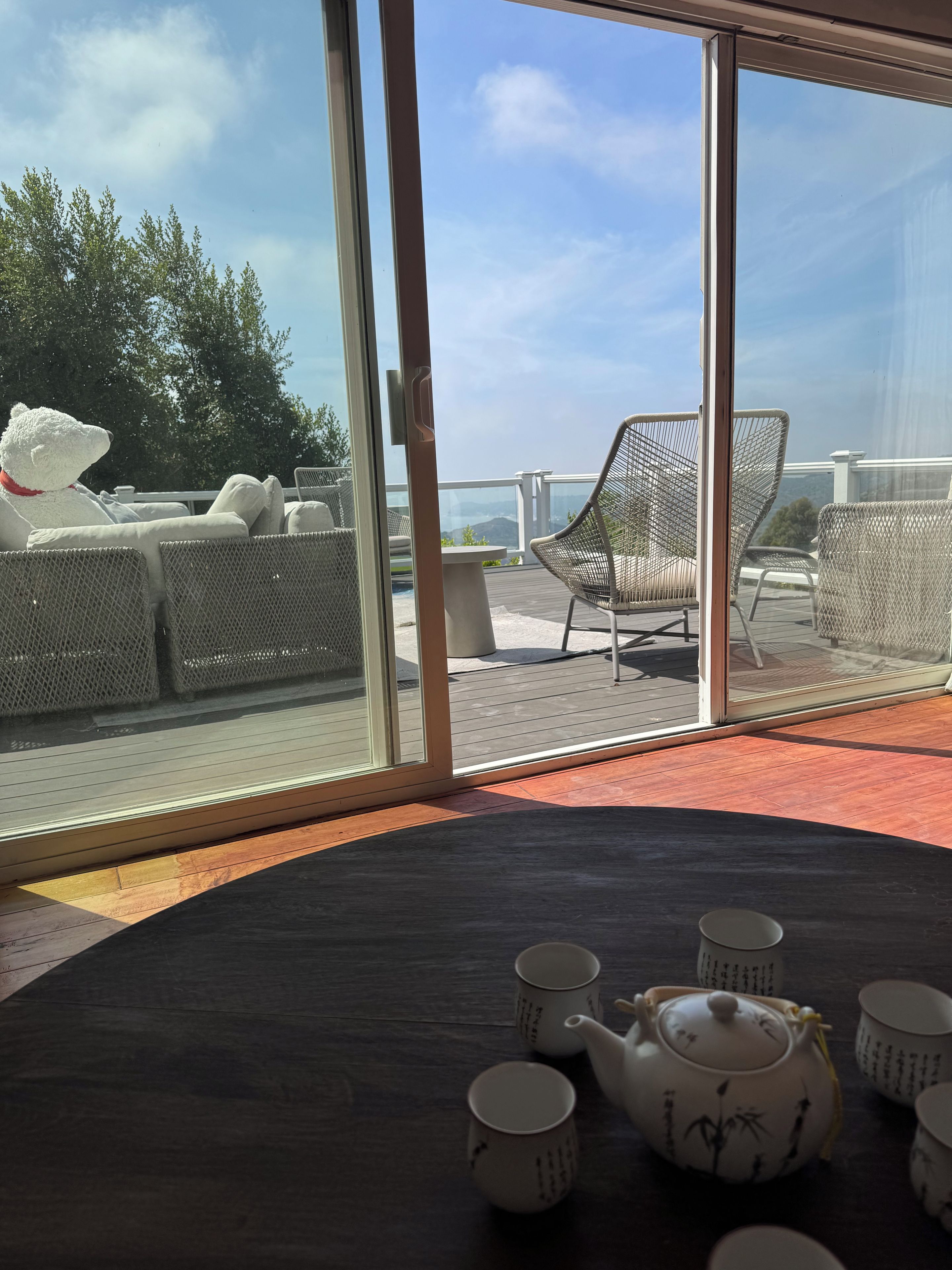 A room with a view of outdoor seating, a table with teapots and cups, and a large glass door.