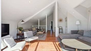A spacious living area with a high ceiling, a sofa set, a coffee table, and a television.