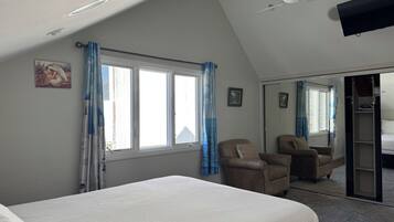 A bedroom with a bed, two chairs, a ceiling fan, and a large mirror.