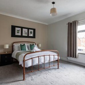 A bedroom with a bed, a nightstand, a lamp, and a window with curtains. - Central Bishop Auckland - House - Sleeps 4 (Bishop Auckland)