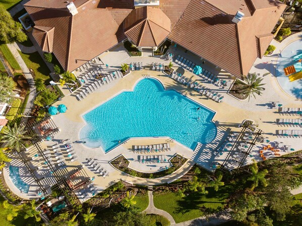 Eine Luftaufnahme eines Resorts mit einem zentralen Schwimmbad, das von Liegebereichen und Palmen umgeben ist.