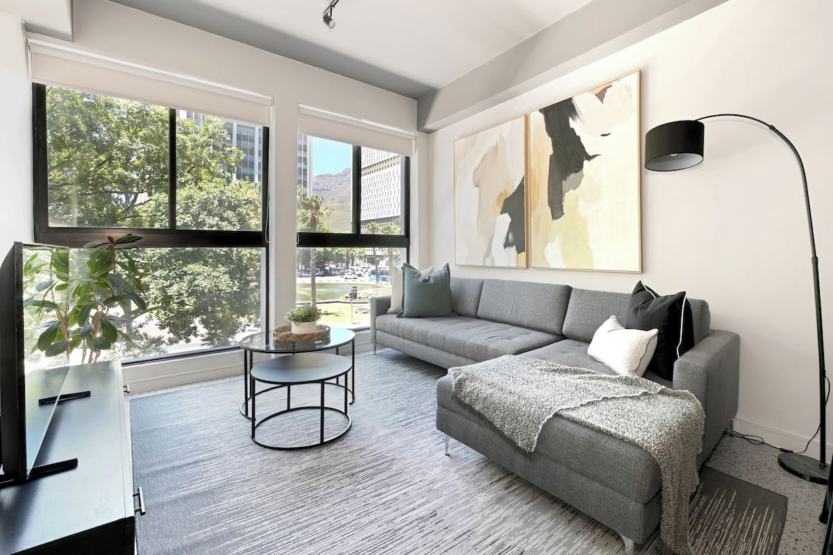 A modern living room with a grey sofa, a coffee table, and a large window offering a view of the city.