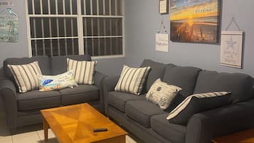 A living room with two sofas, a wooden coffee table, and a window with bars.