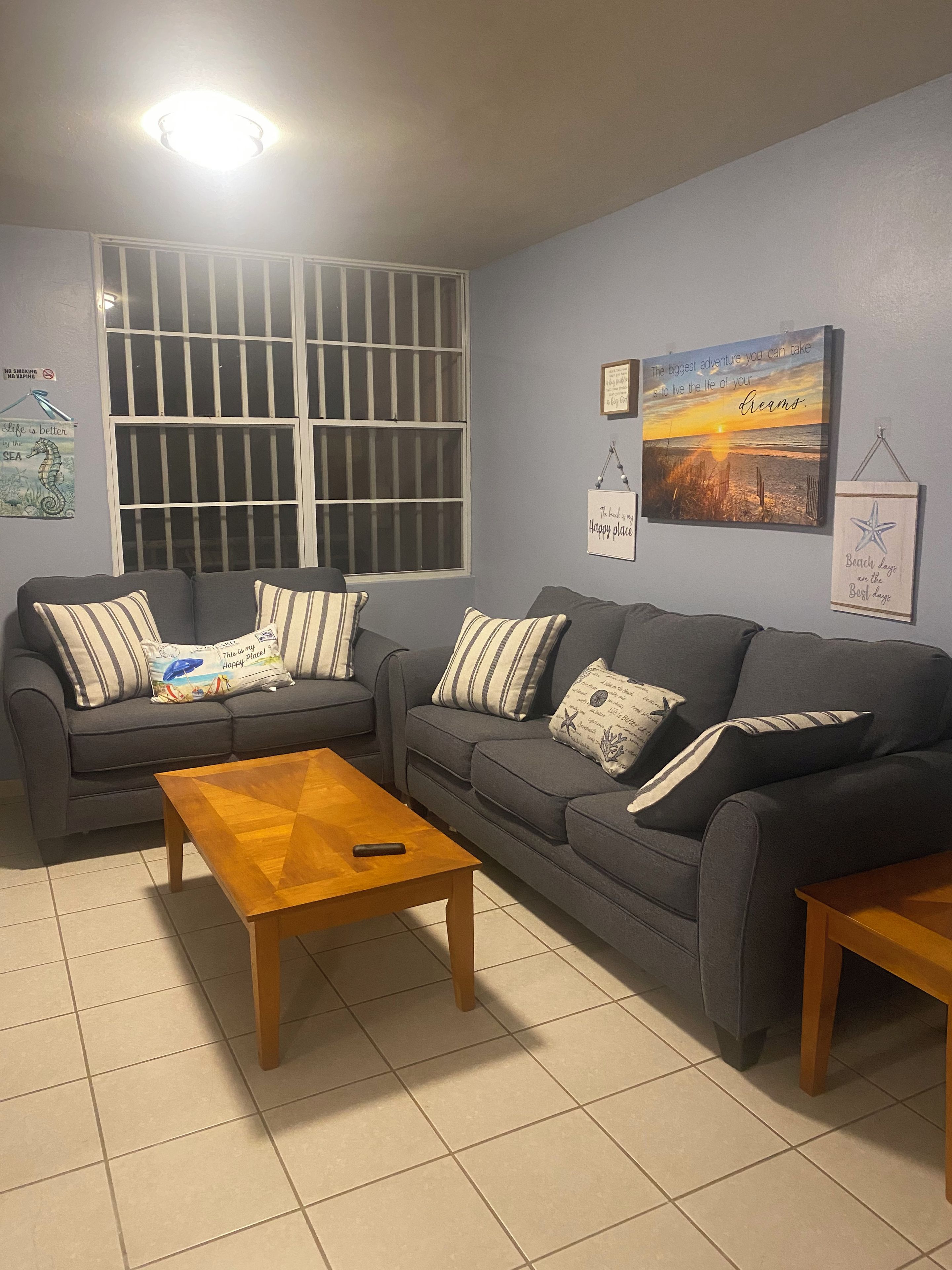 Sala de estar com dois sofás, uma mesa de centro de madeira e uma janela grande com grades.