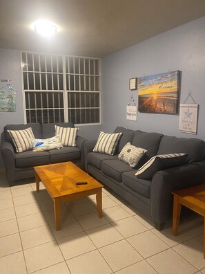 Sala de estar com dois sofás, uma mesa de centro de madeira e uma janela grande com grades.