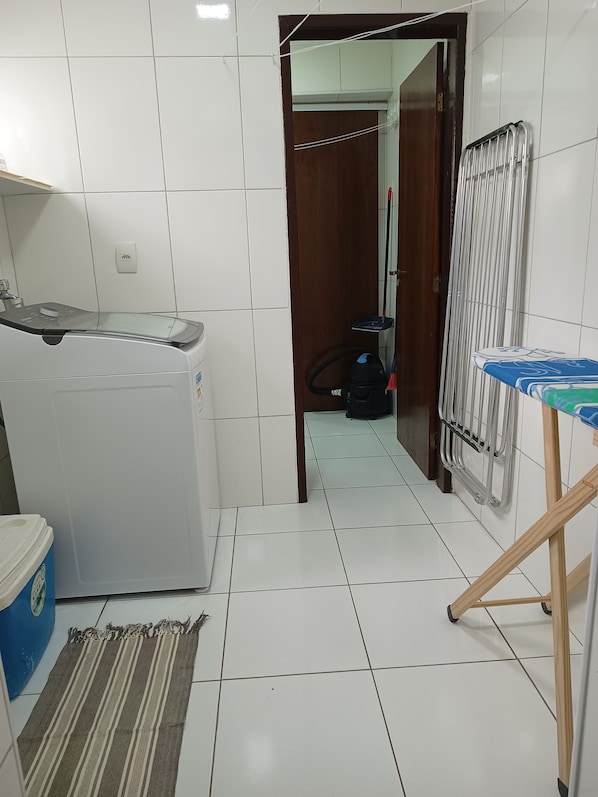 Un espace buanderie comprenant un lave-linge, un étendoir et un aspirateur en arrière-plan.