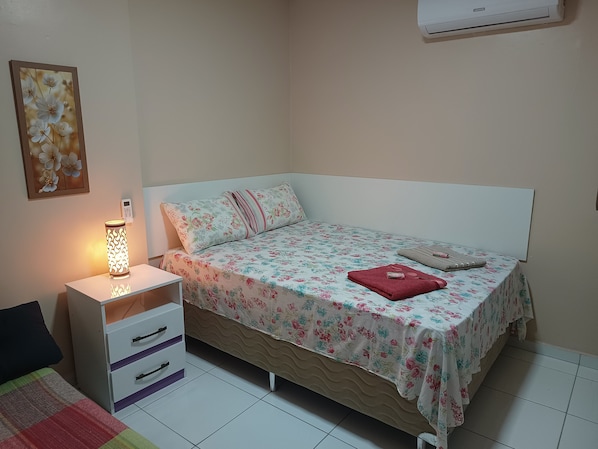 Une chambre à coucher comprenant un lit, une table de chevet, une lampe et un climatiseur fixé au mur.