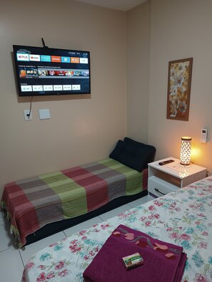 Une chambre à coucher avec un lit, une table de chevet avec une lampe, un téléviseur fixé au mur et un tableau représentant des fleurs.