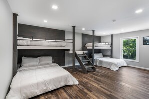 A modern bedroom with bunk beds, a wooden staircase, and a window with a view of trees. - 6BR Poconos Home - Indoor Heated Pool & Hot Tub - Theater, Gym and Game Room (Cresco)