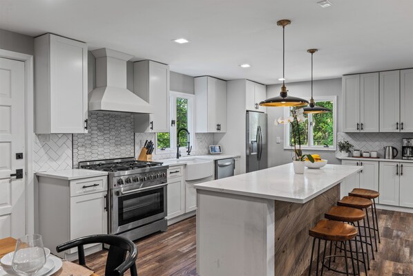 A modern kitchen with white cabinetry, a central island, bar stools, and a stainless steel refrigerator. - 6BR Poconos Home - Indoor Heated Pool & Hot Tub - Theater, Gym and Game Room (Cresco)