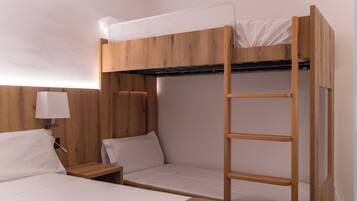 Habitación con literas, cabecera de madera, mesita de noche con lámpara y una escalera.