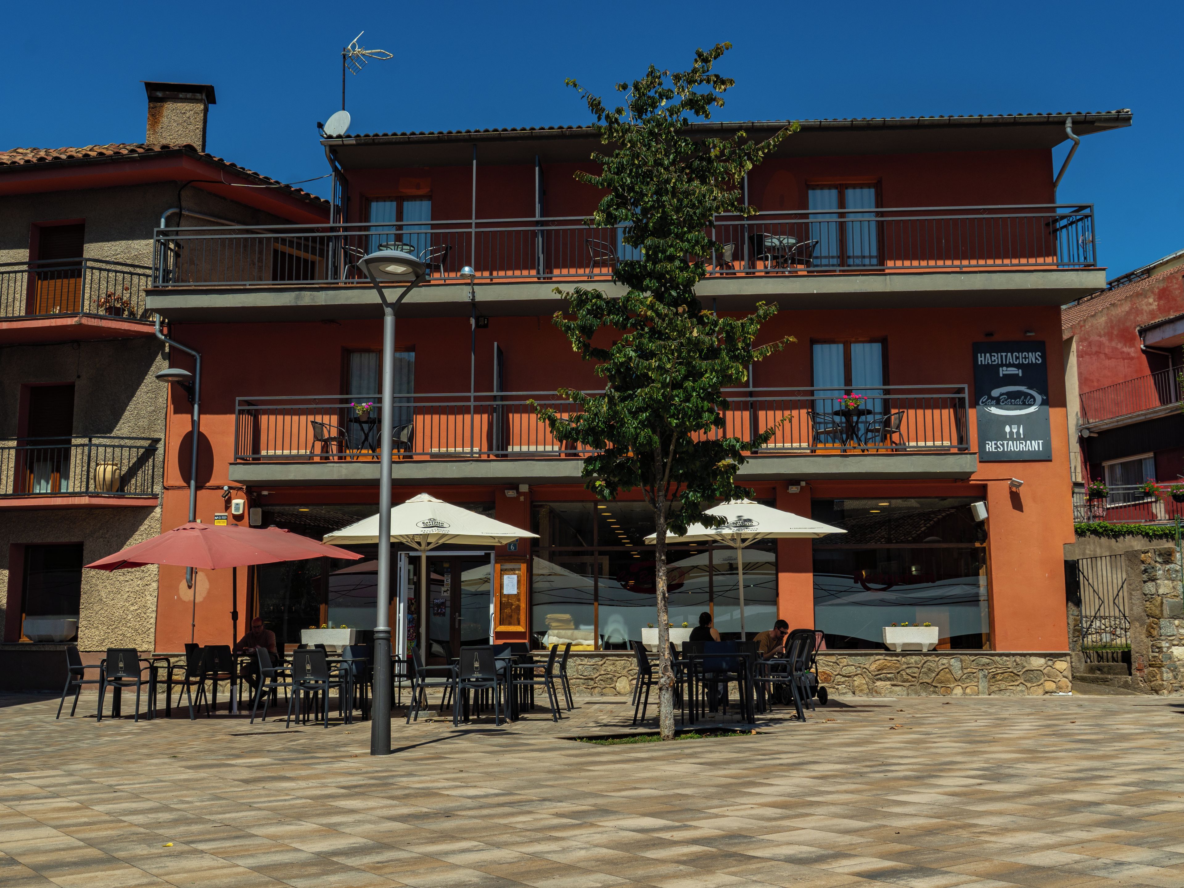 A restaurant with outdoor seating, a signboard, and a building with balconies.