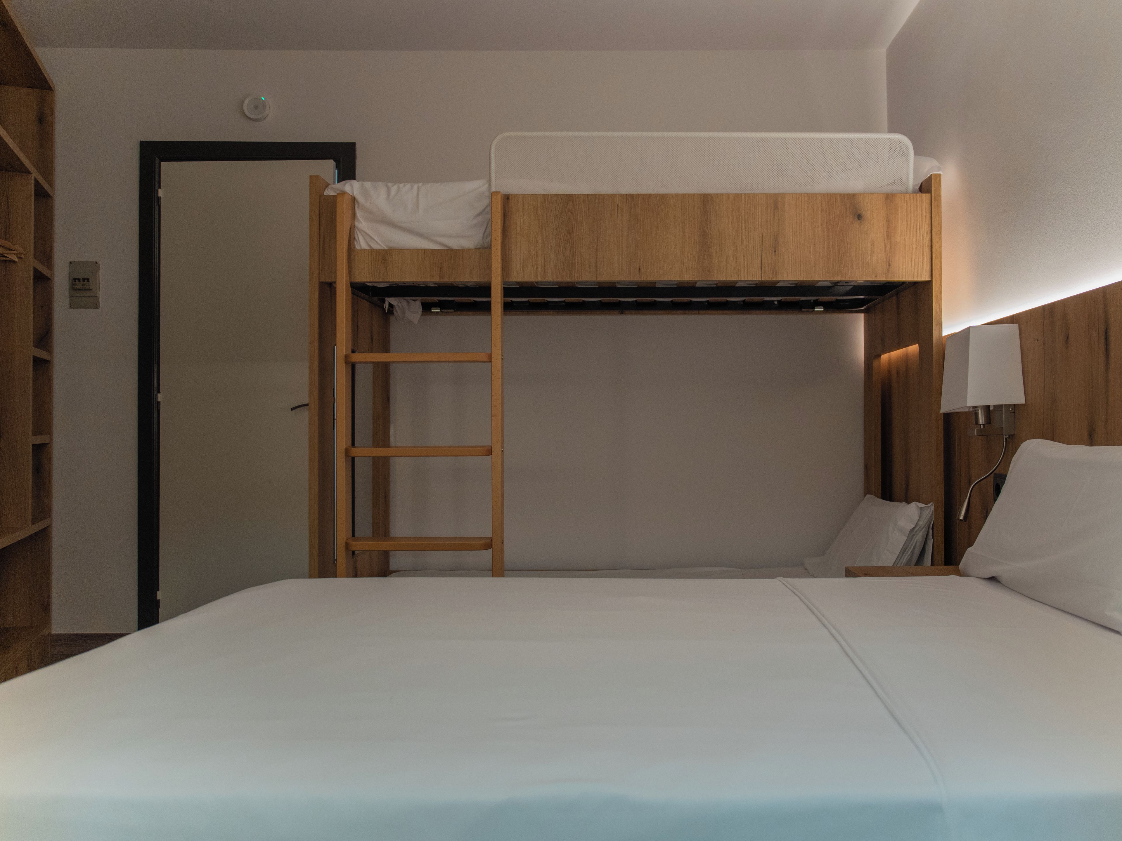 Una cama litera con escalera, una mesita de noche con lámpara y una puerta.