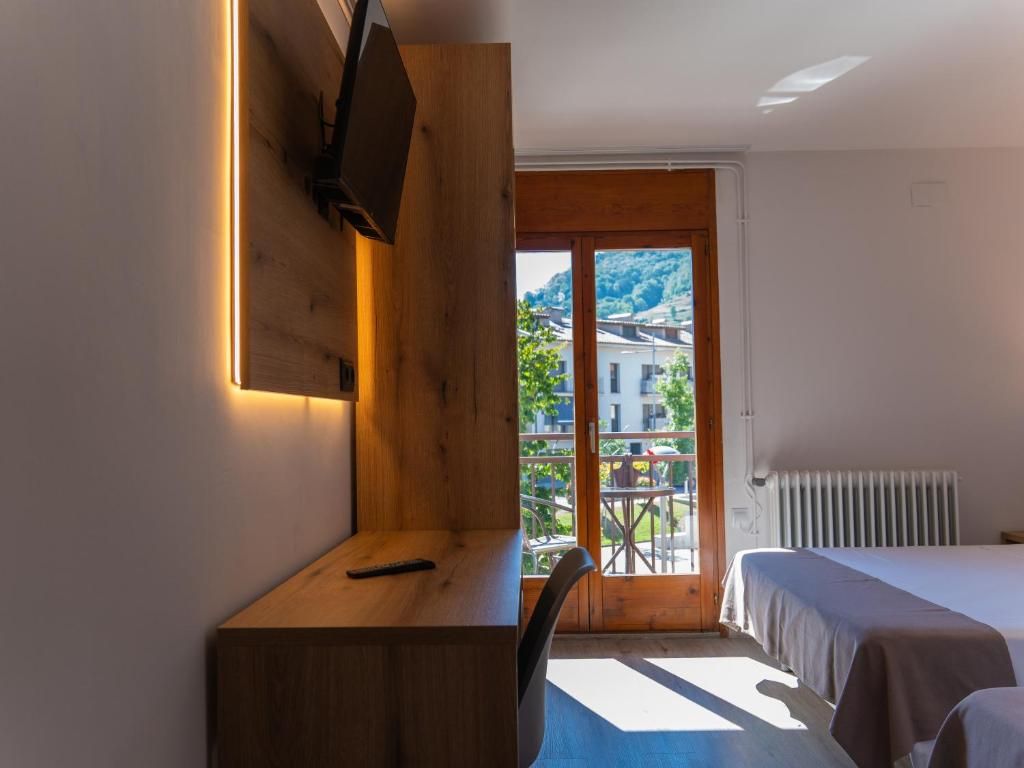 Une chambre d’hôtel équipée d’un lit, d’un bureau, d’un téléviseur fixé au mur et offrant une vue sur l’extérieur grâce à une porte vitrée.