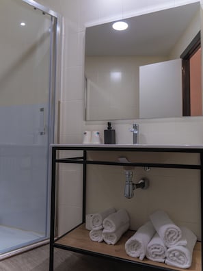 Un baño con cabina de ducha de vidrio, espejo sobre el lavabo y toallas en un estante.