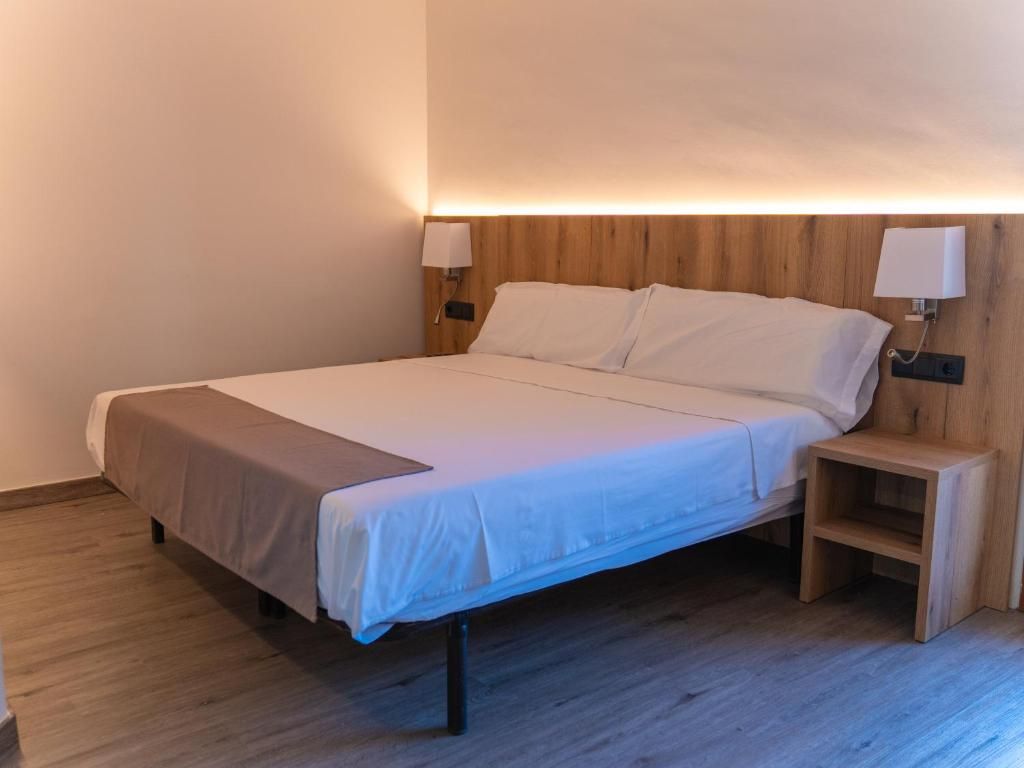 Habitación individual con cama de una sola plaza, cabecera de madera, mesitas de noche y lámparas fijadas a la pared.