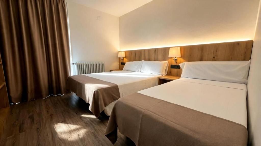 Habitación de hotel con dos camas, suelo de madera, radiador y cortinas.