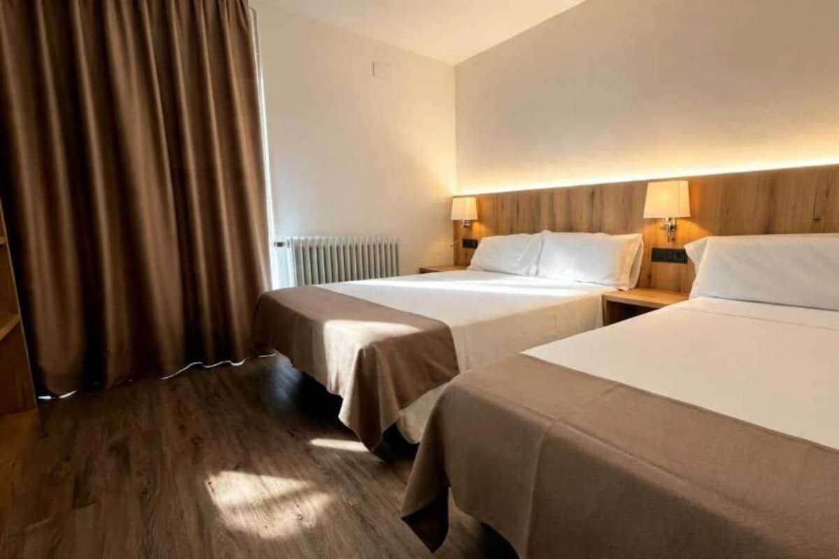 Habitación de hotel con dos camas, suelo de madera, radiador y cortinas.