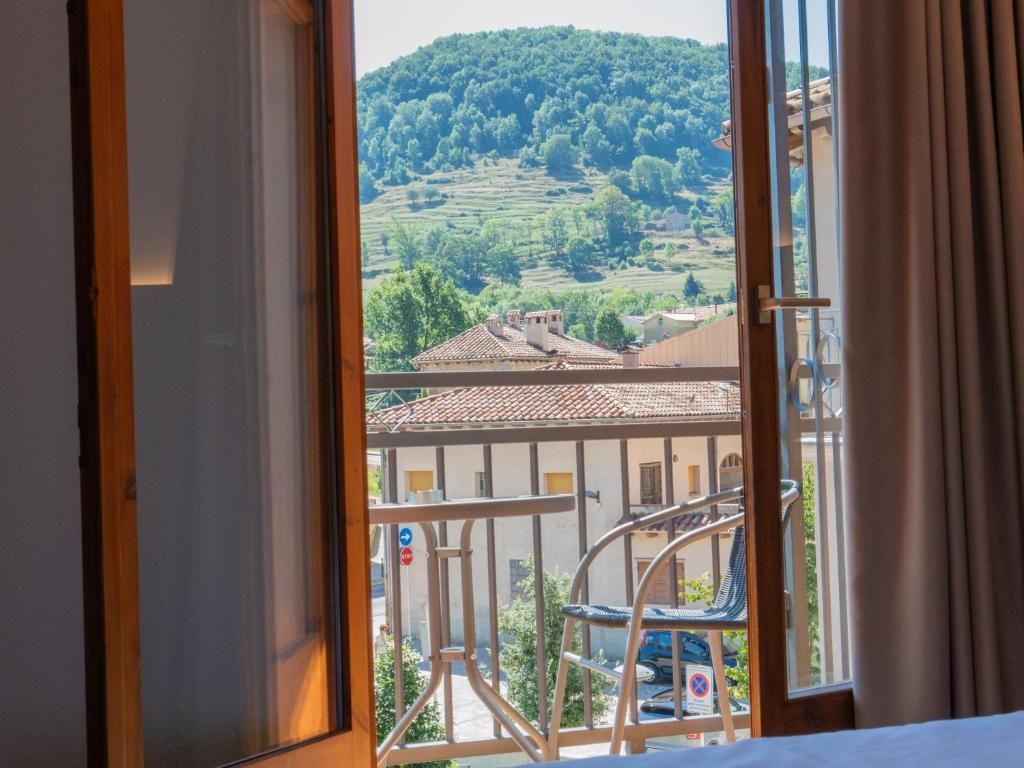 Una habitación con vistas a una colina, un balcón con una silla y un edificio con tejado de tejas.