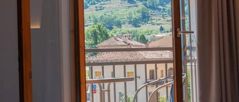 Una habitación con vistas a una colina, un balcón con una silla y un edificio con tejado de tejas.