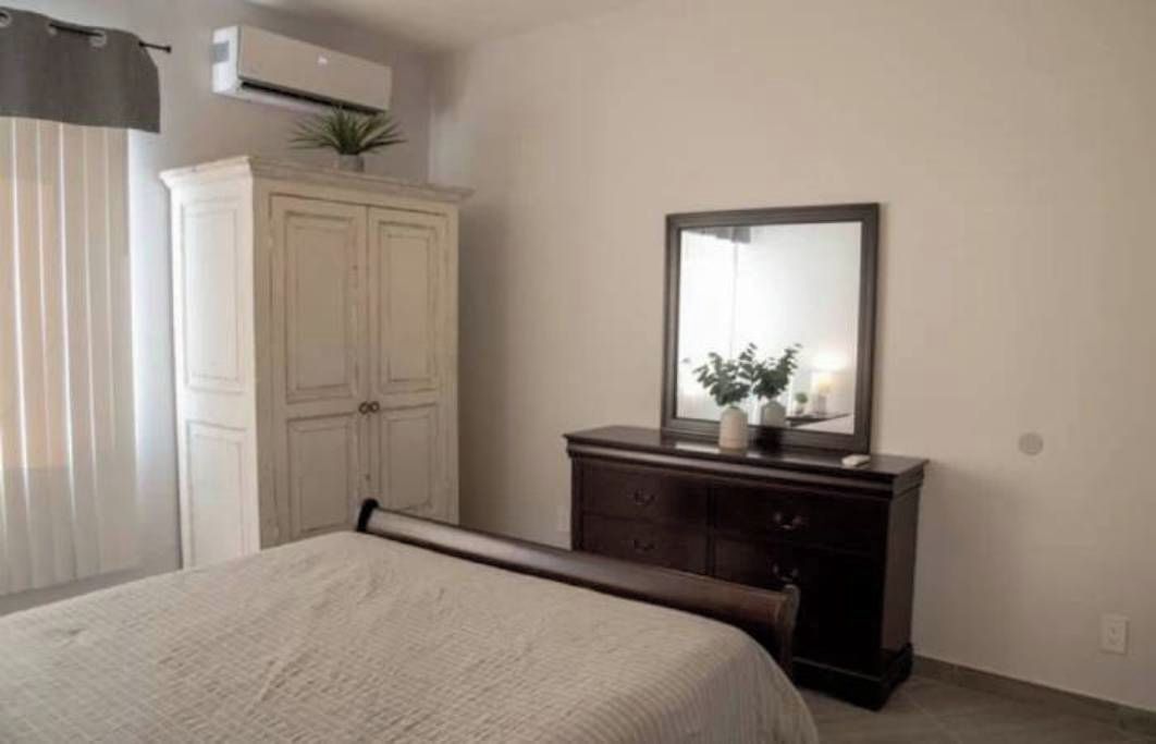 Een slaapkamer met een bed, een dressoir, een spiegel en een raam met gordijnen.