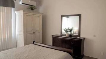 Een slaapkamer met een bed, een dressoir, een spiegel en een raam met gordijnen.