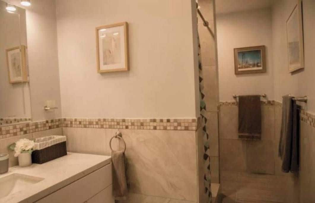Een badkamer met een douche, wastafel en spiegel. Er hangen prenten in lijsten aan de muur.