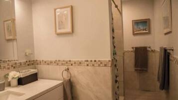 Een badkamer met een douche, wastafel en spiegel. Er hangen prenten in lijsten aan de muur.