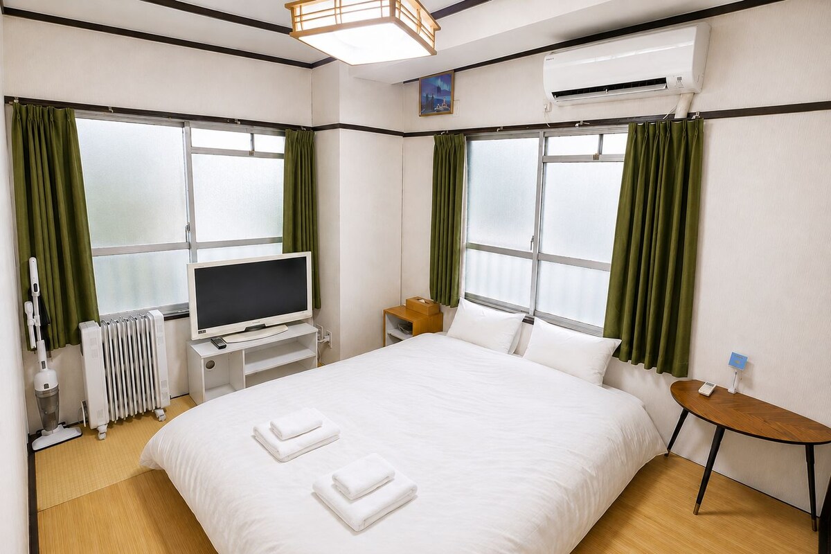 Quarto de hotel com cama, televisão, mesa de cabeceira, abajur e ar condicionado.
