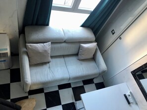 A modern room with a checkered floor, a white sofa with pillows, a small table with a remote control, and a window with curtains. - Vrbo Property (Paris)