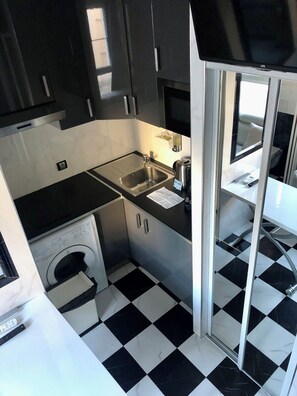 A compact kitchen with a sink, a washing machine, and a small window. - Vrbo Property (Paris)
